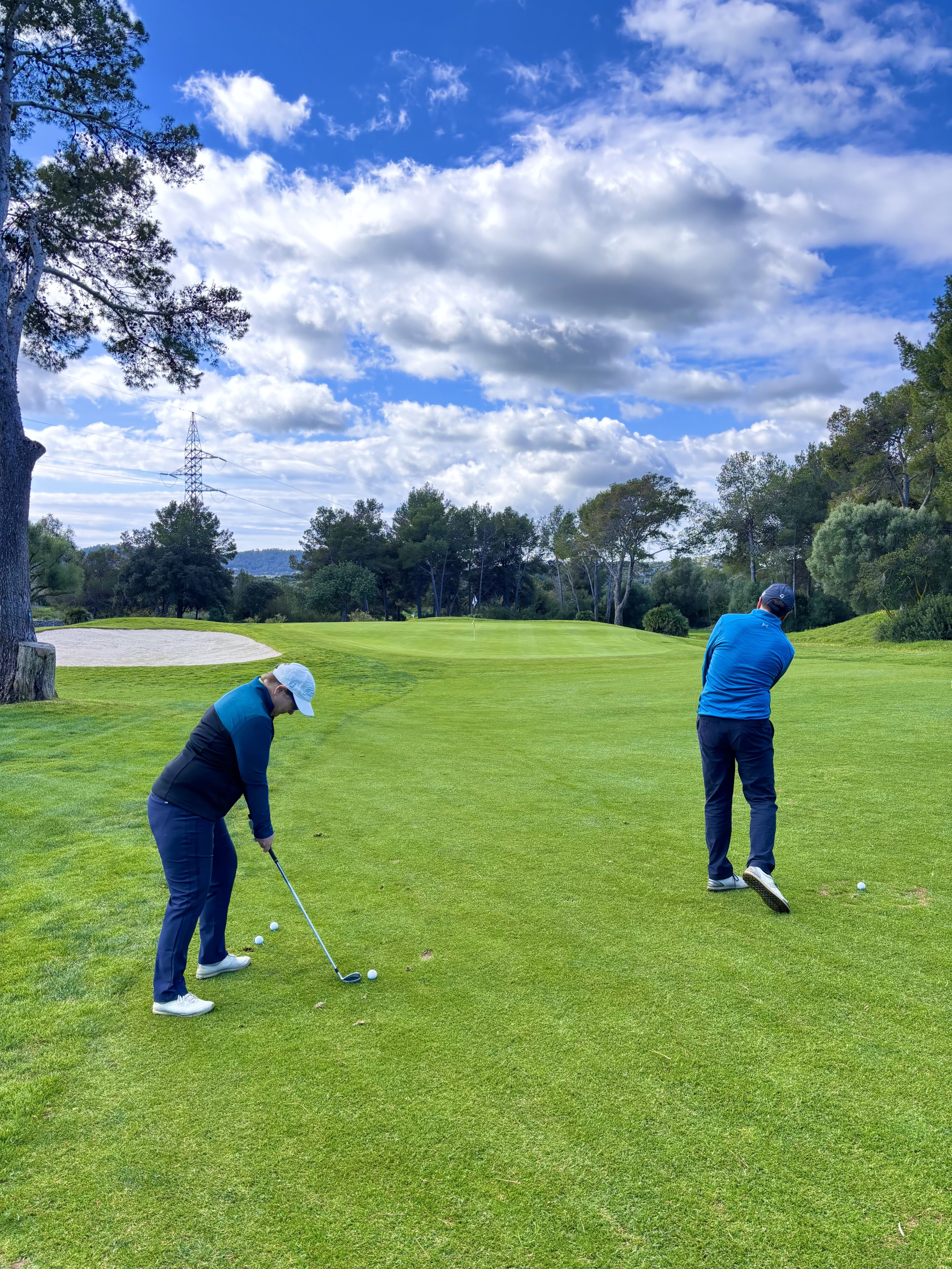 Dos alumnos de golf practicando el approach en el campo, con el profesor observando y dando indicaciones en Capdepera Golf, Mallorca.