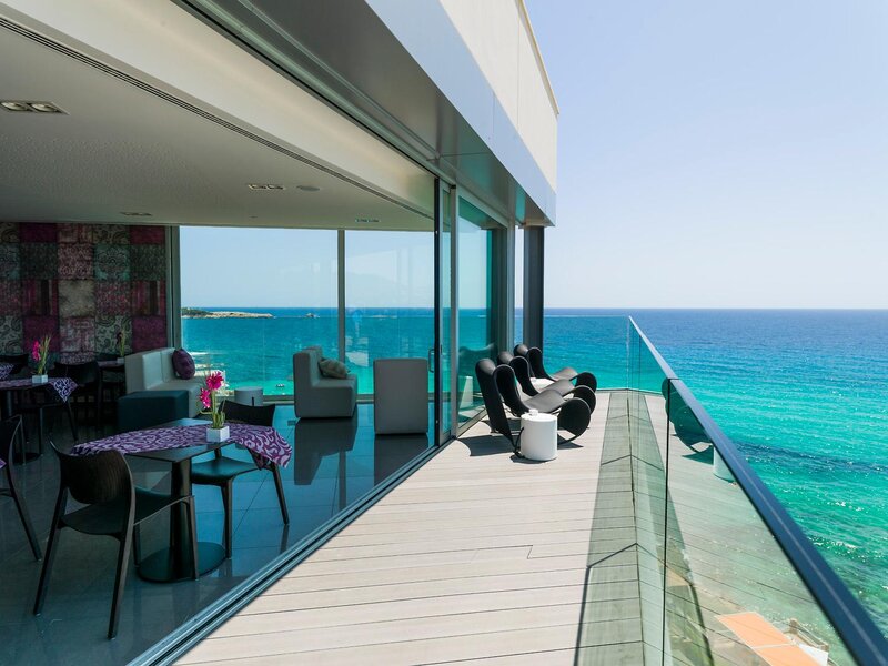 Restaurant Attik im 9. Stock des Sentits Son Moll Hotels mit Terrasse, drei Stühlen und Blick über das türkise Wasser der Son-Moll-Bucht.