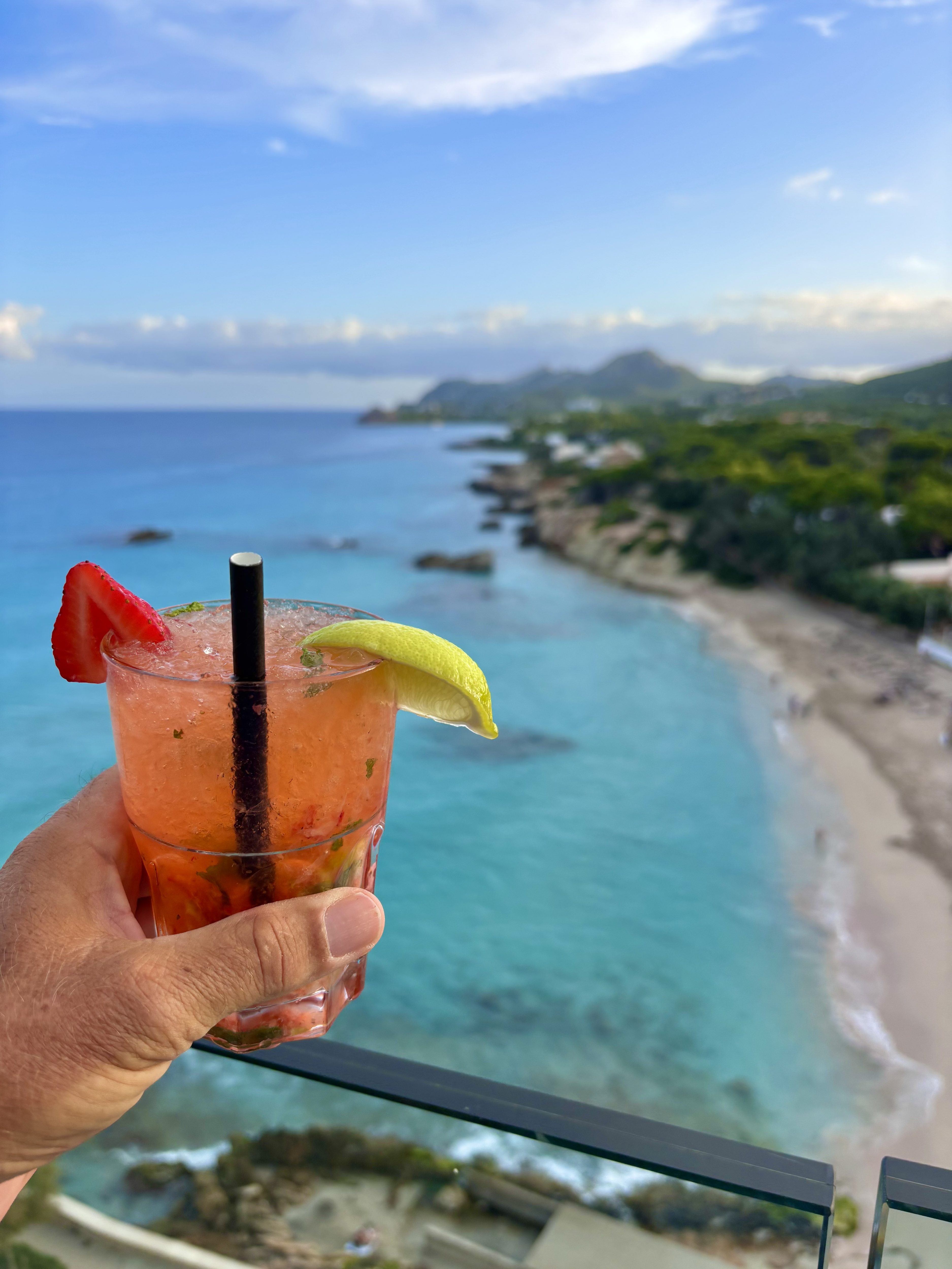 Strawberry Mojito in der Hand mit Blick vom 9. Stock des Attik Restaurants im Sentits Son Moll Hotel auf den Strand von Son Moll und das türkisfarbene Meer in Cala Ratjada.